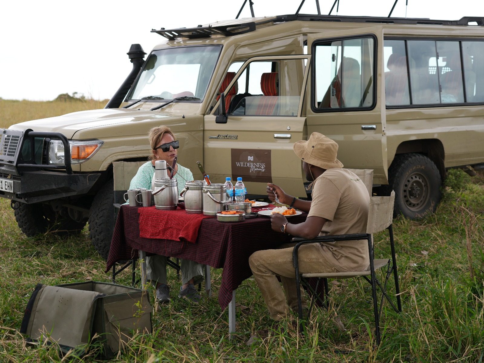 Guide and guest sharing a bush lunch beside the safari vehicle